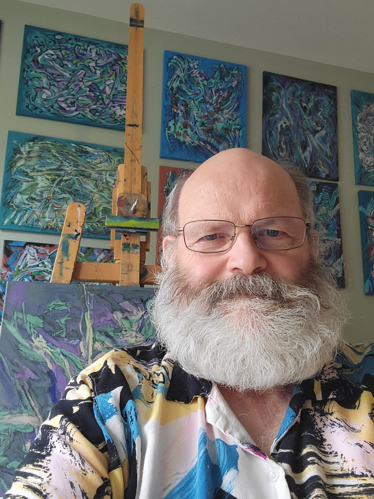 Posing in front of some of the paintings from the 'Out of Your Mind' series (series painted between 2013 and 2015) is the Artist. His shirts sometimes look like they came off his easel. The beard has been a part of his appearance about all of his adult life. Photo was taken in January 2022